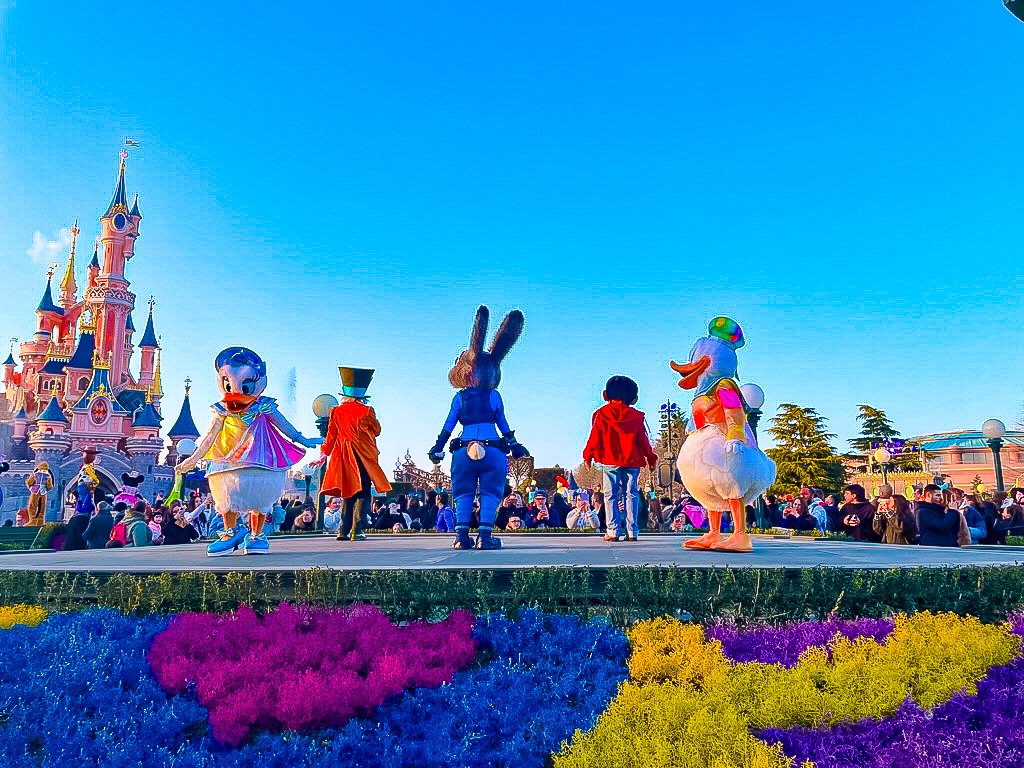 A medley of Disney characters are dancing on stage to the theme tune of Disneyland Paris's 30th anniversary, with the castle in the background and vivid flower beds at the front.