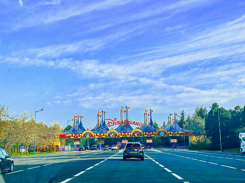 A wide angle shot of the road leading up to the Disneyland Paris carpark entrance. A blue, cloud streaked sky.