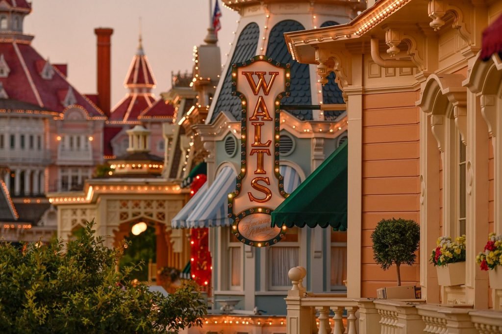 A photograph of the sign for one of the best restaurants in Disneyland Paris, Walt's against the buildings of Main Street in the evening. 